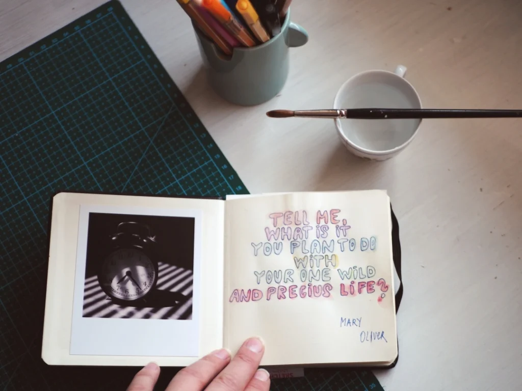 Citát Mary Oliver napsaný ve&nbsp;skicáku vedle fotografie budíku.